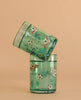 The Konges Sloejd Glitter Cups - Kick It (2 Pack), featuring green-tinted glass with soccer ball and ribbon designs, are stacked together at an angle against a plain beige background—ideal for playful kids' drinkware.