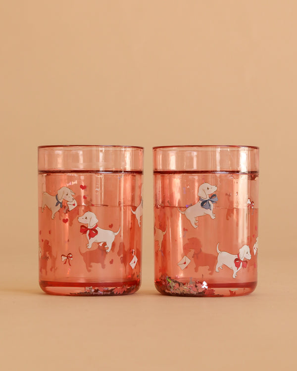 Two Konges Sloejd Glitter Cups - Woof Letter Rose (2 Pack) in pink, featuring playful white dog and bow illustrations—an adorable and fun dinnerware choice for kids.