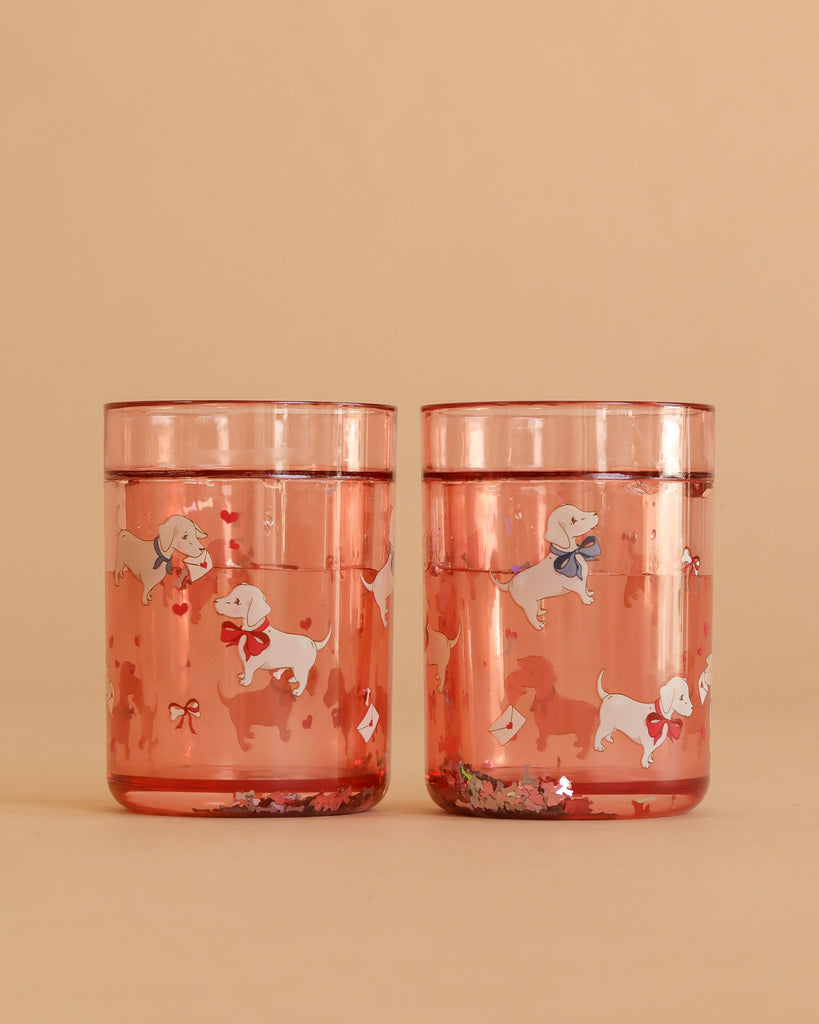 Two Konges Sloejd Glitter Cups - Woof Letter Rose (2 Pack) in pink, featuring playful white dog and bow illustrations—an adorable and fun dinnerware choice for kids.