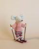 A small, stuffed toy mouse stands upright on red skis with wooden ski poles. The mouse is dressed in a pink knit sweater and plaid pants, with white felt hands and feet. This charming Maileg Christmas Winter Mouse With Ski Set, Big Sister set against a neutral beige background adds a cozy touch to any playset.
