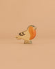 The Handmade Holzwald Finch Bird, featuring an orange breast, beige body, and dark accents, stands on a flat surface against a peach background—ideal for anyone seeking sustainable toys.
