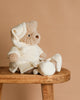 The Mon Ami Briar Bedtime Bear Plush Toy, dressed in a cream robe, nightcap, and plush slippers, sits on a wooden bench against a beige background—the ideal bedtime companion.