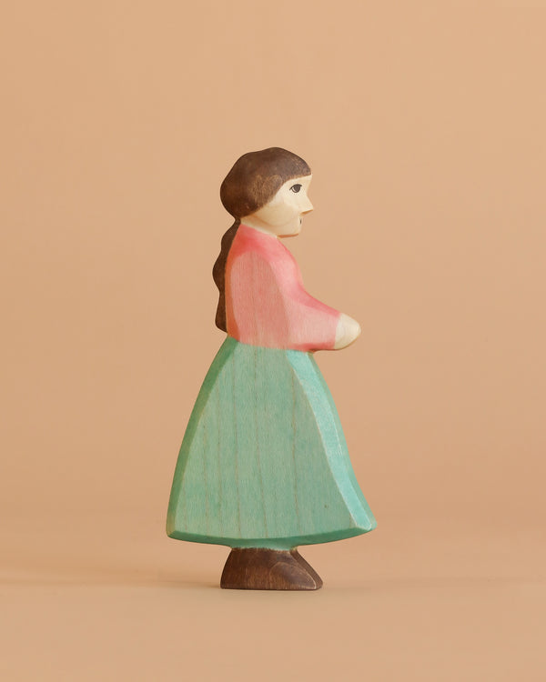 The Handmade Holzwald Goose Girl is a wooden figurine with brown hair, a red top, and teal skirt, shown in profile against a beige background—ideal for imaginative play and fans of sustainable wooden toys.