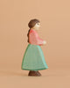 The Handmade Holzwald Goose Girl is a wooden figurine with brown hair, a red top, and teal skirt, shown in profile against a beige background—ideal for imaginative play and fans of sustainable wooden toys.