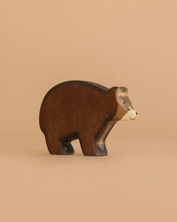 A Handmade Holzwald Bear with a brown body and lighter tan face stands against a plain beige background, highlighting the charm of sustainable toys.
