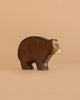 A Handmade Holzwald Bear with a brown body and lighter tan face stands against a plain beige background, highlighting the charm of sustainable toys.