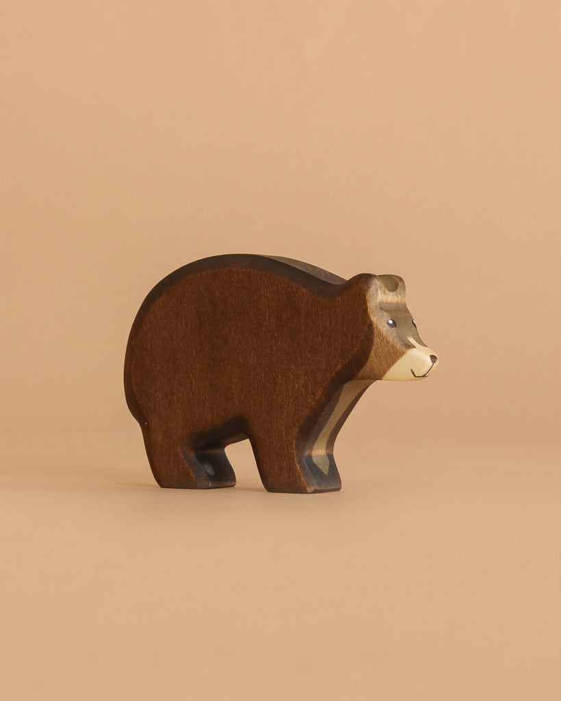 A Handmade Holzwald Bear with a brown body and lighter tan face stands against a plain beige background, highlighting the charm of sustainable toys.