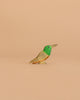 The Handmade Holzwald Hummingbird, a small wooden figurine painted green, yellow, and brown, is centered against a plain beige background, highlighting the charm of sustainable toys.