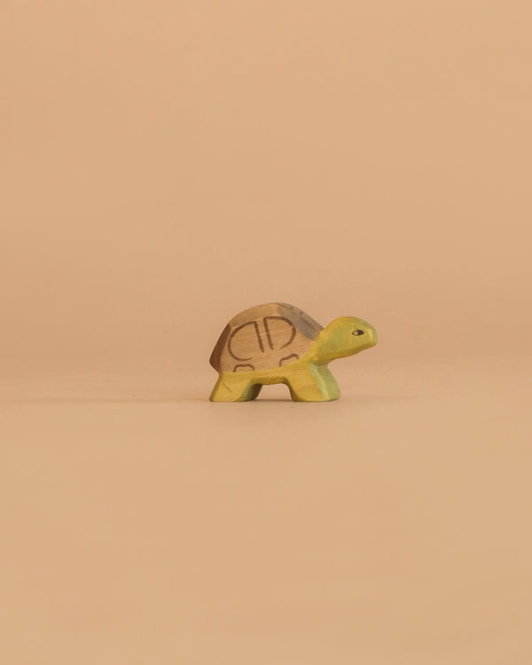 The Handmade Holzwald Small Turtle, a green and brown wooden figurine, rests on a plain beige background—perfect for those who appreciate sustainable toys.