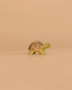 The Handmade Holzwald Small Turtle, a green and brown wooden figurine, rests on a plain beige background—perfect for those who appreciate sustainable toys.