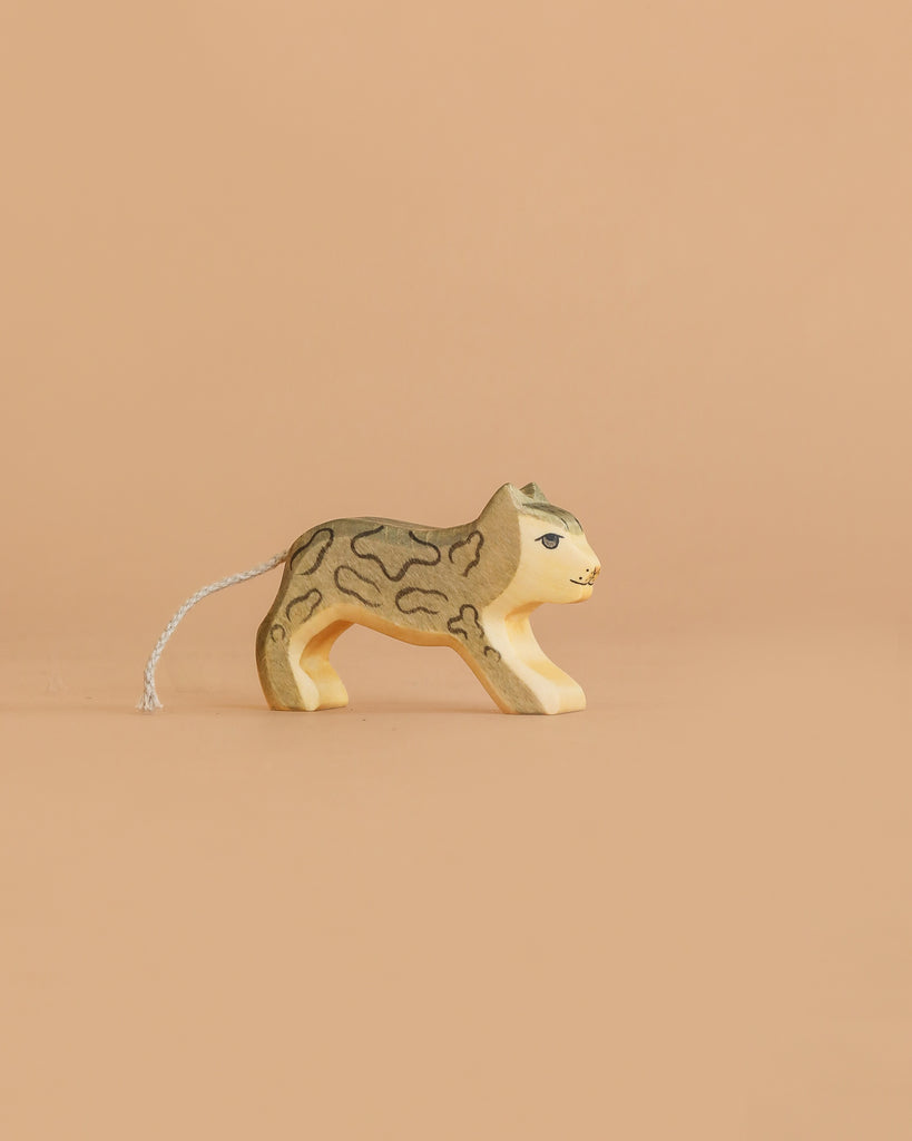 The Handmade Holzwald Small Snow Leopard is a wooden toy with painted details and a string on its back, ideal for imaginative play and photographed on a plain beige background.