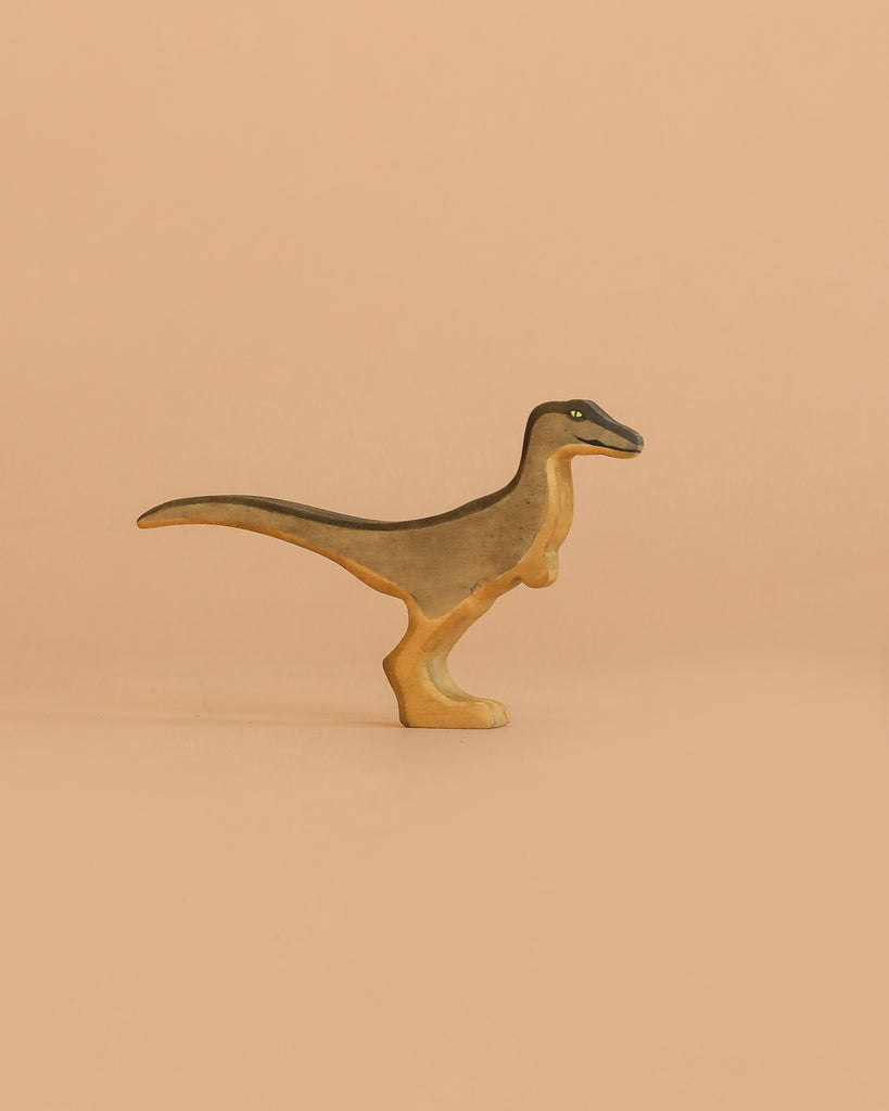 The Handmade Holzwald Velociraptor, a small wooden figurine with short arms and a long tail, stands upright against a light brown background—ideal for fans of sustainable toys.