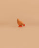 The Bumbu Handmade Wooden Brown Hen, crafted from sustainable Romanian wood and hand-painted in brown shades, is displayed on a smooth, light orange background.