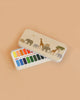 The Konges Sloejd Water Colors Paint Set - Safari is a rectangular tin box with a beige lid showing elephants, giraffes, and a tree. Inside are two rows of vibrant rectangular paint pans.
