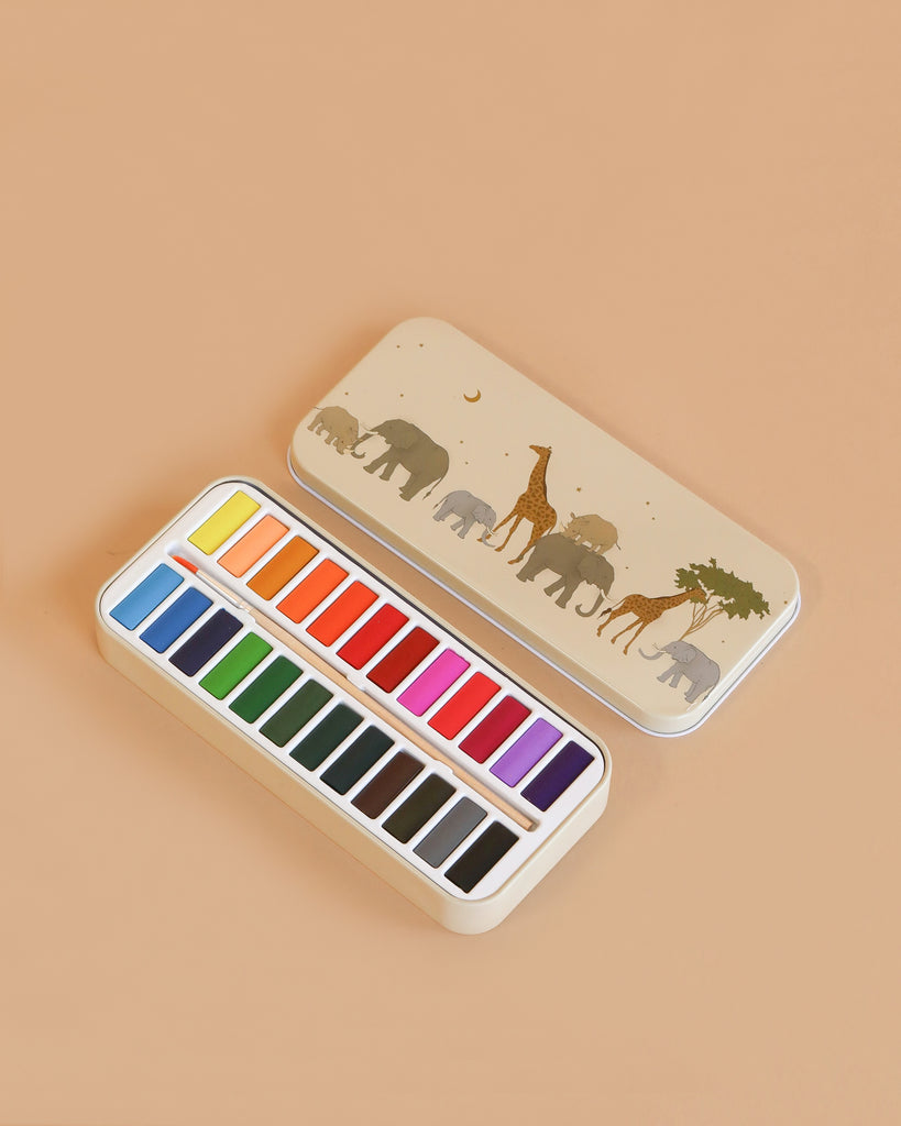 The Konges Sloejd Water Colors Paint Set - Safari comes in a beige tin box with elephant and giraffe art under a night sky. Inside are 18 vibrant rectangular pans, perfect for use with your favorite wooden paint brush.