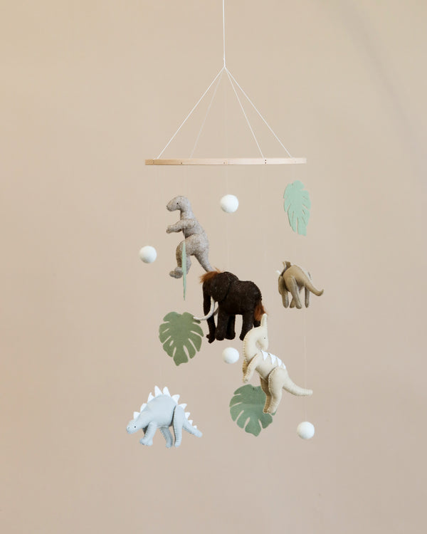 A Handmade Mobile - Dinosaur - Final Sale featuring plush dinosaur toys and green felt leaves hanging from wooden sticks against a light beige background, designed to support visual development.