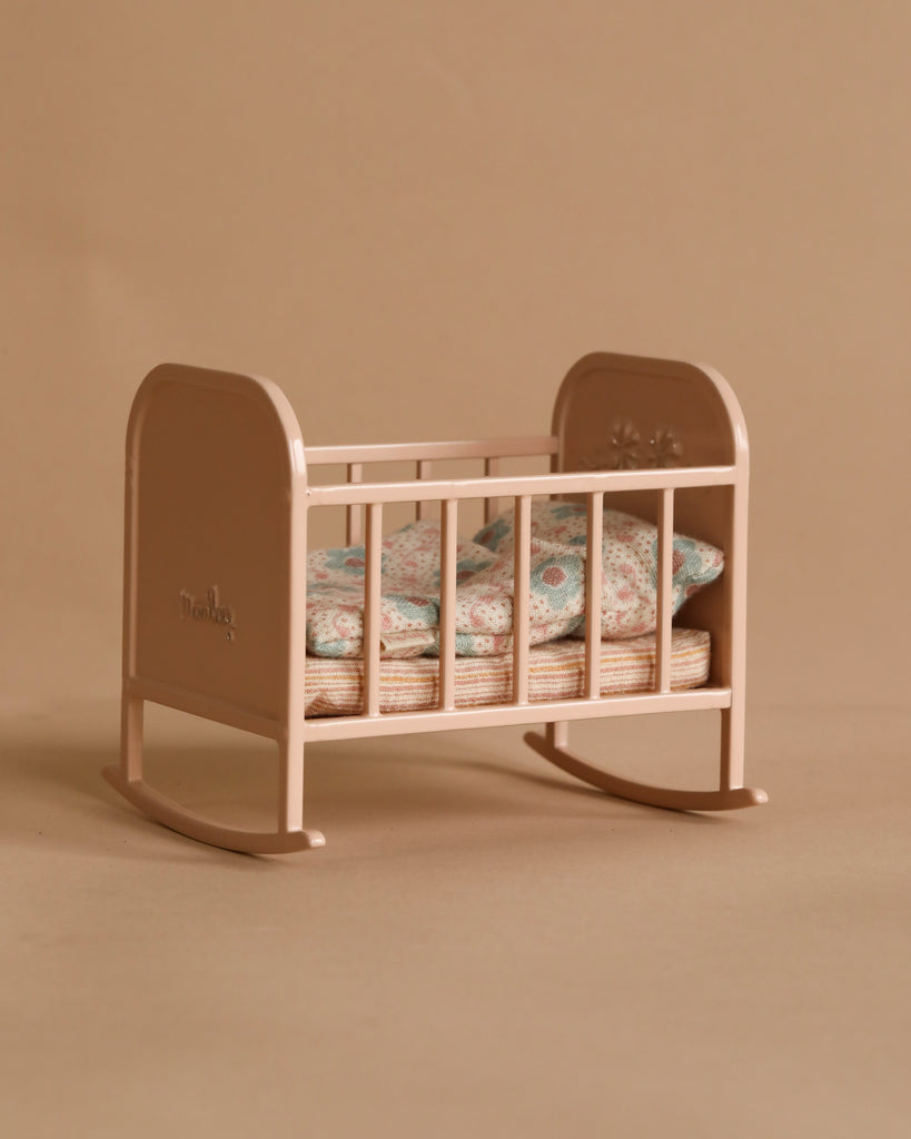 The Maileg My Cradle - Light Rose, with its beige base and floral-patterned bedding, features a small rocking mechanism. A soft sleeping bag introduces color, enhancing the neutral hues. Its classic, simple, and elegant design completes the timeless look.