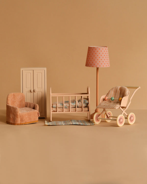 The Maileg Nursery Set, featuring a cozy armchair, crib with bedding, stroller, rug, lamp with polka dot shade, and wardrobe in harmonious beige and pastel tones, is a charming addition perfect for the tiny mouse family.