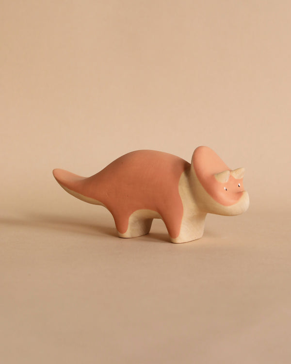 A handmade wooden Triceratops dinosaur crafted from linden wood and pink non-toxic paint, displayed against a soft beige background.