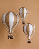 Three decorative handmade Hot Air Balloon - Gold ornaments, featuring alternating white and beige panels with small brown baskets, are suspended against a solid beige background—perfect for charming children’s room decoration.