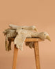 Two Senger Naturwelt Cuddly Animal Linen Geese, made from organic materials, are stacked atop each other on a wooden stool set against a plain beige background.