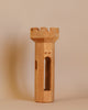 The Ostheimer Round Tower is a smooth, light wood carving that stands upright. This handcrafted wooden toy features an arched window cut through its center and a notched top resembling castle battlements, perfect for imaginative play. The background is a plain, neutral beige.