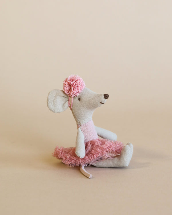 A small, handmade Maileg Ballerina Mouse - Little Sister (Rose) dressed in a pink ballet outfit, including a tutu and a tiny flower on its ear, sitting upright against a plain beige background. This little sister mouse is poised like