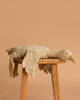 The Senger Naturwelt Cuddly Animal - Linen Goose, made with soft GOTS-certified cotton, rests on a wooden stool against a plain light brown background.