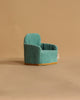 A small, teal miniature armchair with gold trim from the Maileg Family Time Living Room Set is shown on a plain beige background. With plush upholstery and a rounded backrest, it's perfect as mouse dollhouse furniture.