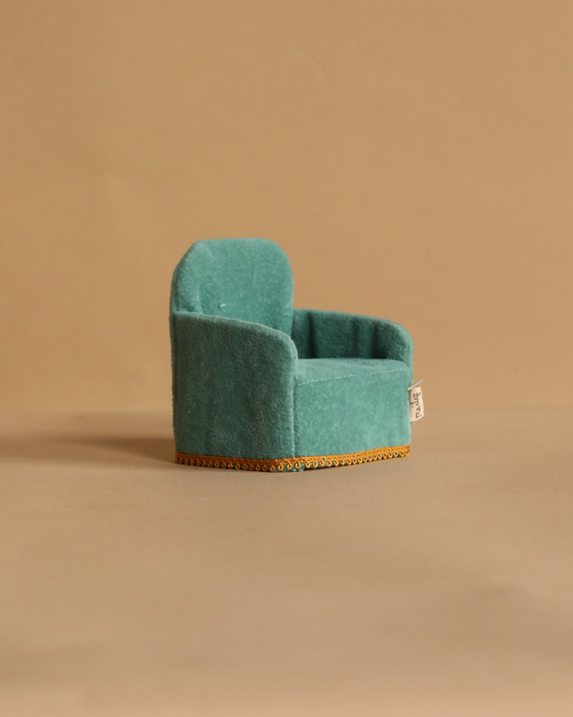 A small, teal miniature armchair with gold trim from the Maileg Family Time Living Room Set is shown on a plain beige background. With plush upholstery and a rounded backrest, it's perfect as mouse dollhouse furniture.