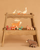 The Holztiger Handmade Wooden Woodland Animals Set features ducks, a deer, squirrels, rabbits, and two bears displayed on a two-tiered wooden stand, perfect for open ended play against a beige background.