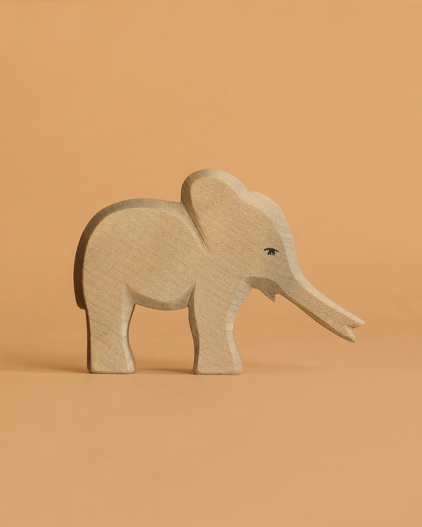 The Ostheimer Small Elephant - Trunk Out is a handcrafted wooden figurine with subtle carved details, set against a plain light orange background—perfect for imaginative play or as part of an Ostheimer toys collection.