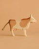 The Ostheimer Cow - Standing is a handcrafted wooden figurine with light brown and cream patches, a twine tail, and simple carved features, showcasing sustainable design in toys.