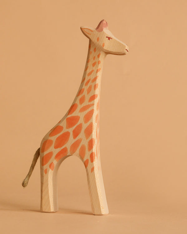 The Ostheimer Giraffe - Standing features orange spots, a white face, and a gray tail. Handcrafted from wood, it stands against a beige background—ideal for imaginative play.