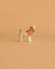 A small, handcrafted goat from the Ostheimer Handmade Wooden Farm Animals Set, featuring light brown and white hues, stands on a beige surface—showcasing charming toys made from sustainably sourced wood.