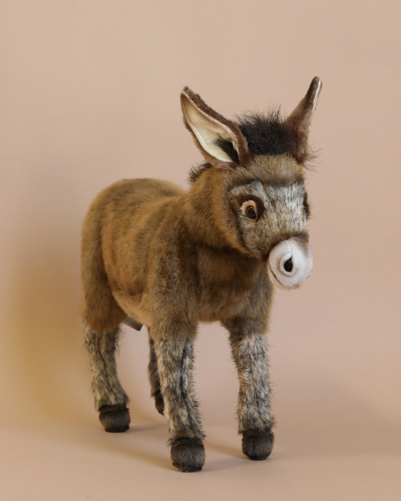 The Donkey Stuffed Animal, featuring a brown body, gray legs, and a dark tuft of fur on its head, stands against a neutral beige background. This handcrafted plush toy showcases large, expressive eyes and long, upward-pointing ears.