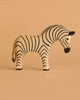 The Ostheimer Zebra is a handcrafted wooden figurine with black stripes, standing on a beige surface against a matching background—ideal for imaginative play.