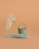 The Maileg Big Brother Gone Fishing Set, featuring a green toy bucket, matching fishing net with a wooden handle, and a soft fabric fish, is displayed on a plain beige background.