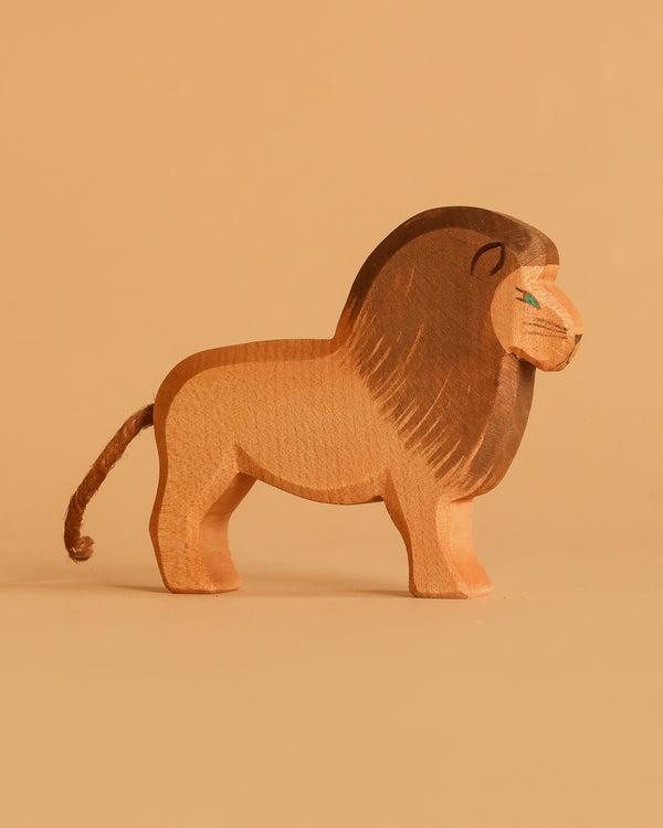 The Ostheimer Lion - Male is a handcrafted wooden toy with a brown mane and tail, blue eye detailing, and a simple design. It stands on a beige surface against a beige backdrop, perfect for imaginative play and classic in style.