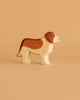 The Ostheimer Handmade Wooden Farm Animals Set features a handcrafted wooden toy dog with brown and white markings, made from sustainably sourced materials, standing upright against a plain beige background.