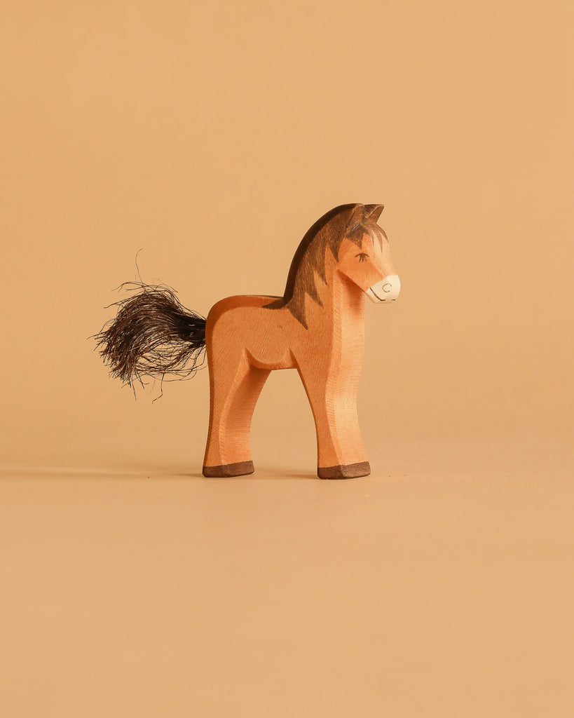 The Ostheimer Brown Horse / Colt, a handcrafted wooden toy with a painted mane and tail, stands on a beige surface against a matching background—an enduring example of sustainable play.