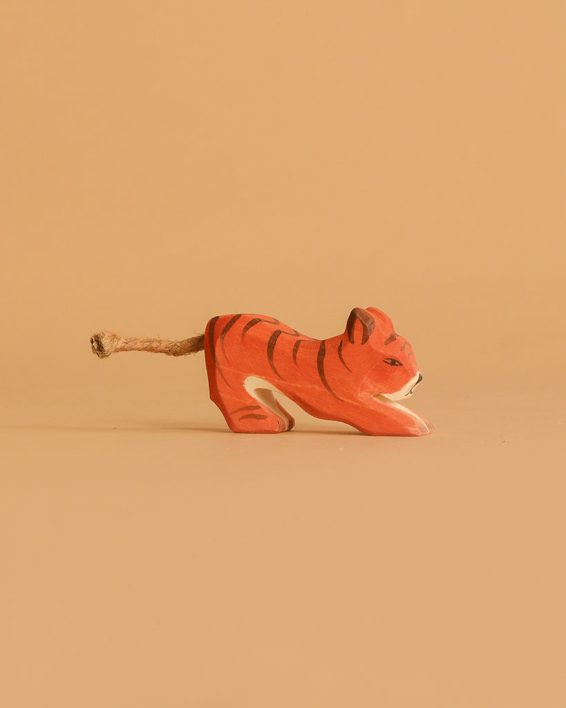 An Ostheimer Handmade Wooden Safari Animals Set tiger, small and hand-painted with a rope tail, is displayed against a plain light brown background, highlighting the charm of handcrafted toys.
