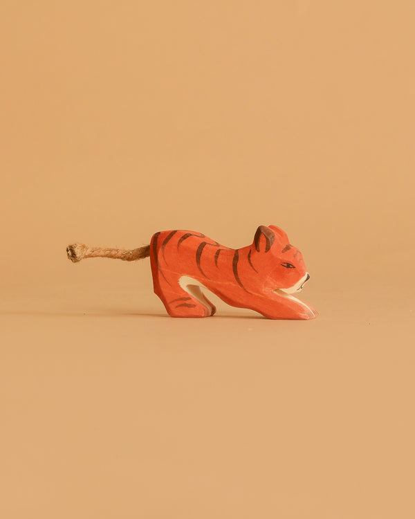 The Ostheimer Tiger Lurking, Small is a handcrafted wooden figurine with orange and black stripes and a rope tail, shown on a plain beige background.