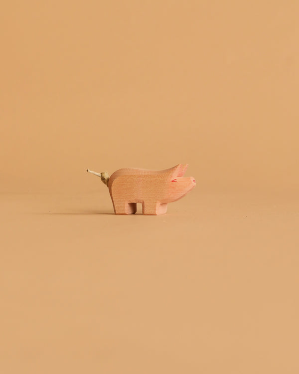 The Ostheimer Piglet, a small minimalist wooden figurine with a twig tail, is centered on a solid beige background—ideal for imaginative play.