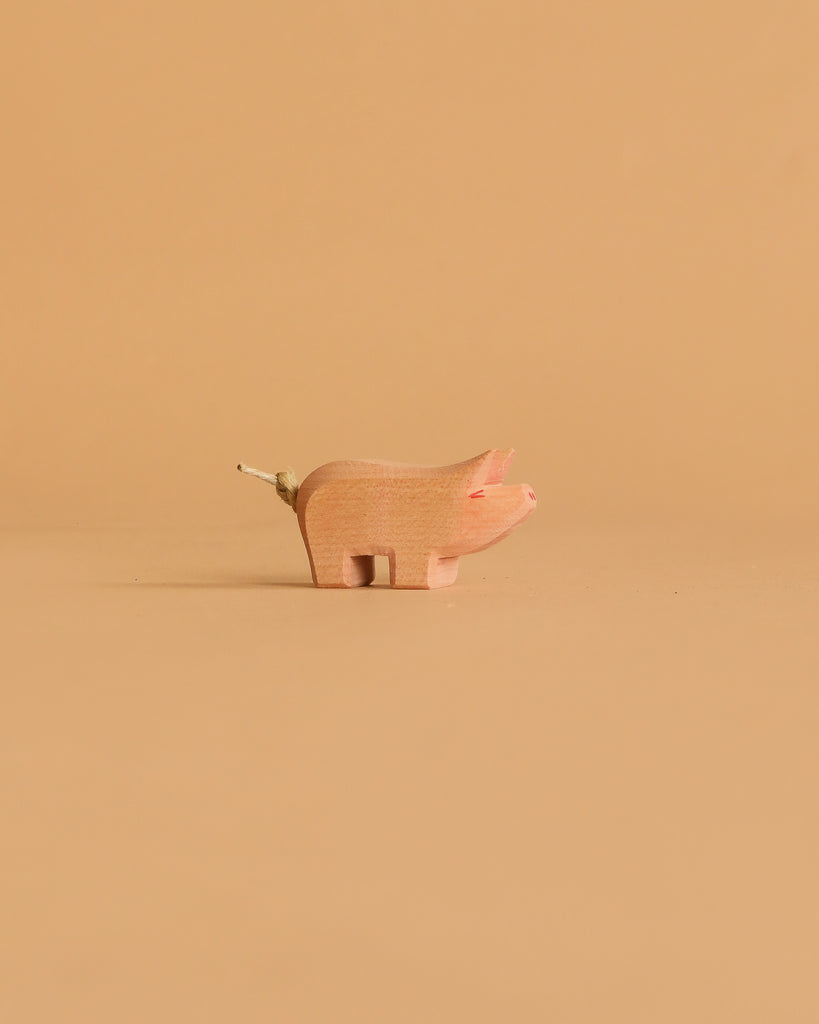 The Ostheimer Piglet, a small minimalist wooden figurine with a twig tail, is centered on a solid beige background—ideal for imaginative play.