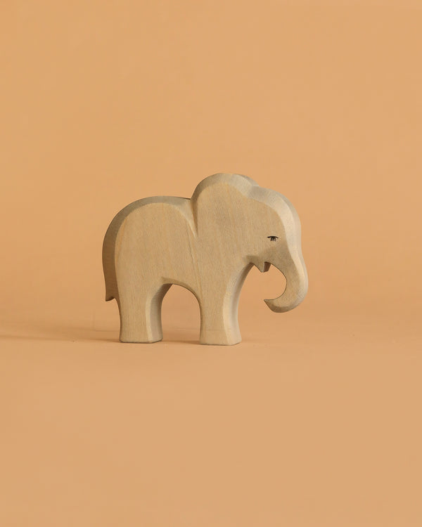 The Ostheimer Small Elephant - Eating is a light-toned wooden figurine with smooth edges and minimal carved details, perfect for imaginative play. It stands simply on a beige background, showcasing its minimalist design.