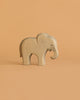 The Ostheimer Small Elephant - Eating is a light-toned wooden figurine with smooth edges and minimal carved details, perfect for imaginative play. It stands simply on a beige background, showcasing its minimalist design.