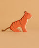 An Ostheimer Handmade Wooden Safari Animals Set tiger figurine, crafted from wood with painted black stripes and a rope tail, is shown against a simple beige background.
