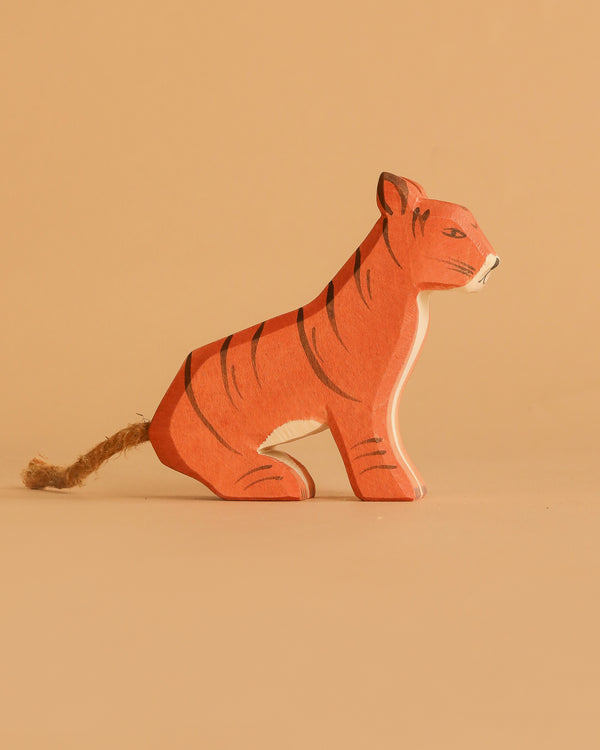 The Ostheimer Sitting Tiger is a small, handcrafted wooden figurine featuring black stripes and a rope tail, displayed on a plain beige background.