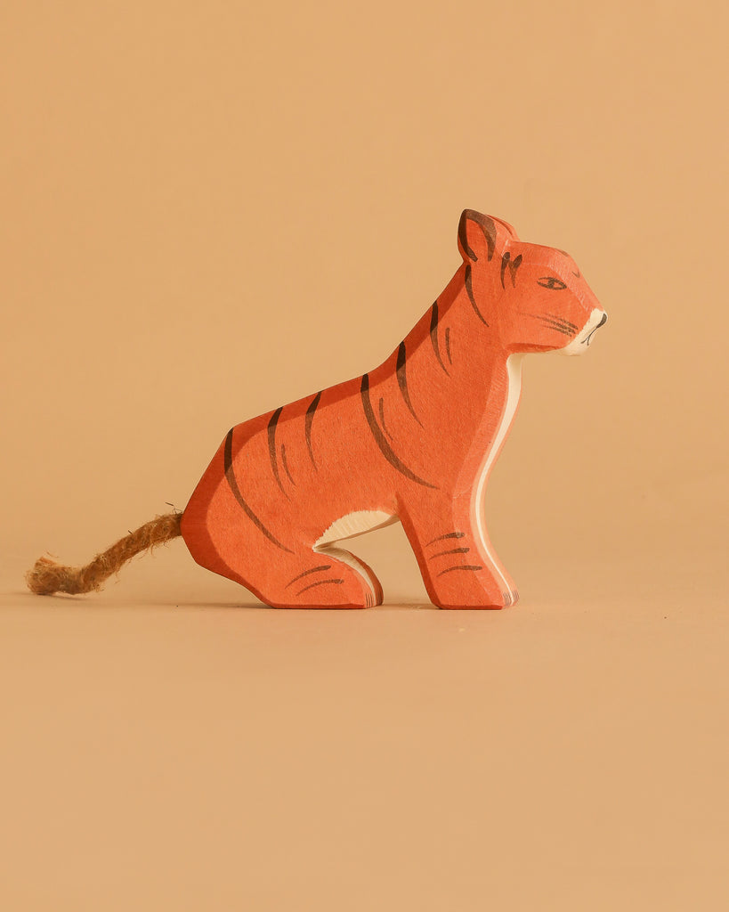 The Ostheimer Sitting Tiger is a small, handcrafted wooden figurine featuring black stripes and a rope tail, displayed on a plain beige background.